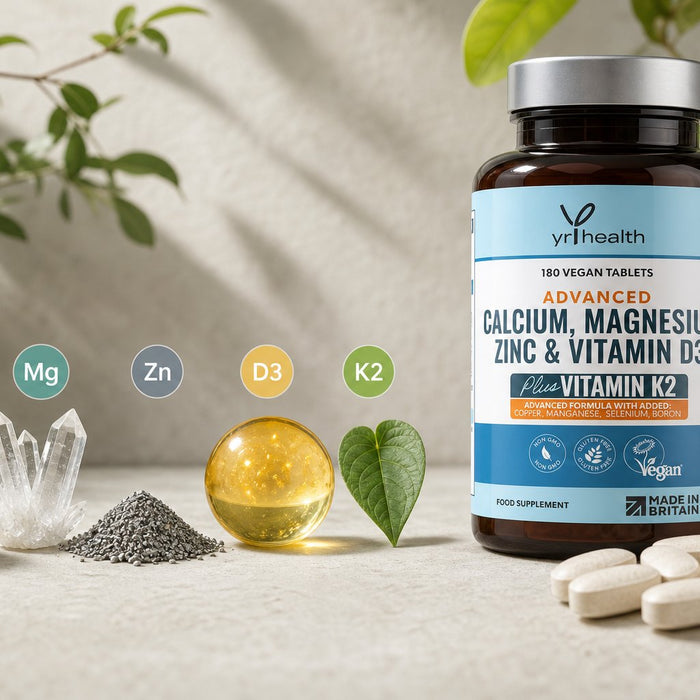 Supplement bottle beside tablets, crystals, a mineral pile, a golden sphere, and a green leaf on a light tabletop with leafy plants in the background.